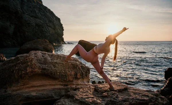 Young woman with black hair, fitness instructor in pink sports leggings and tops, doing pilates on yoga mat with magic pilates ring by the sea on the beach. Female fitness daily yoga concept