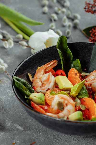 Shrimps salad with cherry tomatoes, cucumeber, avocado, lettuce and pomegranate on dish. Healthy seafood concept. Tasty grilled prawn shrimp and mix vegetable salad on black, top view.