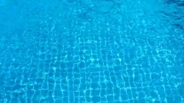 Dalgalı havuz suyu, parlak mavi arka plan ve ızgaralı döşeme döşemesi.