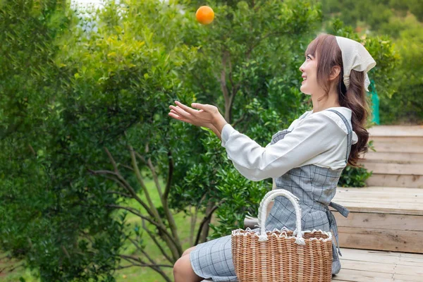 Elbiseli genç bir kadın portakal bahçesinde oturuyor. Bir sürü portakal ağacı ve sepetli bir elden portakal fırlatıyor. Bahçede mutlu mesut çalışan çiftçi konsepti