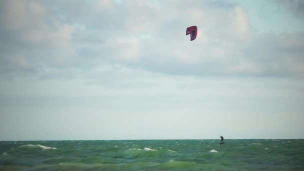 Kitesurfing a smaragd tenger hullámain. A férfi kiteboardozik a türkiz tengervízben. A férfi a táblán gyorsan átúszik a hullámokon. Nyári szünet. — Stock videók