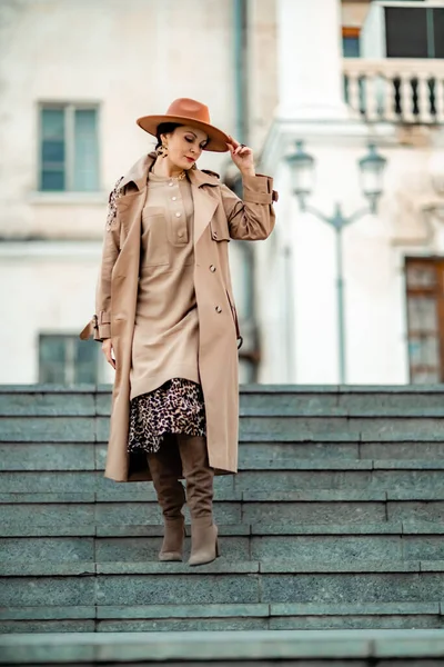 Retrato de moda al aire libre de la joven mujer morena elegante de moda, modelo en sombrero elegante, gargantilla y impermeable ligero posando al atardecer en la ciudad europea. — Foto de Stock