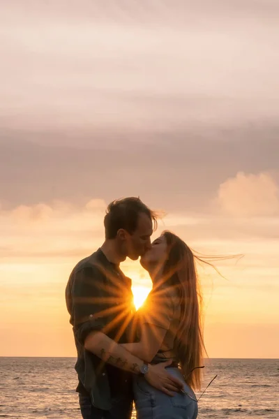 Silhouettes in love romantic couple lovers hugging, kissing, touching, eye contact at sunset, sunrise on the background of the sea, the sun, the clouds in fiery red, orange colors — Stock Photo, Image