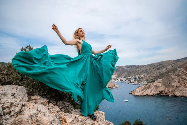 Zümrüt elbiseli bir kadın, uzun ipek kanatlı, dalgalı elbiseli bir manken, setin üzerinde uçan kumaş.. — Stok fotoğraf