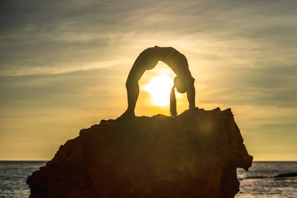 Девушка гимнастка тренируется на пляже на закате моря. Делает бечевку. Серия фотографий. — стоковое фото