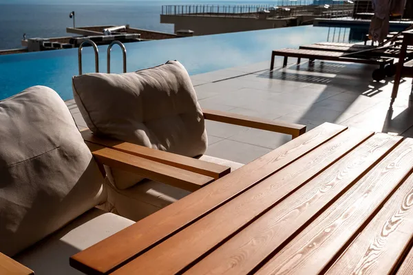 Restaurante com vista para o mar. Você pode ver pedras no mar. Mesas de madeira e cadeiras com almofadas brancas. nublado, tempo nublado. — Fotografia de Stock