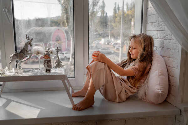 Resting and thinking girl in pajamas sitting on the window-sill at home. Side view.