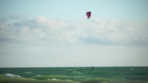 Kitesurfen op de golven van de smaragdgroene zee. De man is aan het kitesurfen in het turquoise zeewater. De man op het bord zweeft snel door de golven. Zomervakantie. — Stockvideo