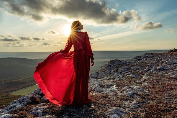El ascenso de la mística. puesta de sol sobre las nubes con una chica en un vestido rojo largo. Se encuentra en la montaña con una vista mágica. —  Fotos de Stock
