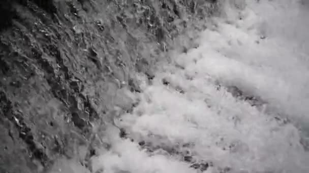 Slow Motion, Close Up: Krachtige razende witwaterwaterval die krachtig over een rotsachtige rand valt. Kristalhelder gletsjerwater dat over de klif stroomt. — Stockvideo