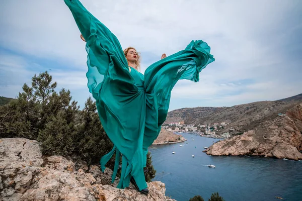 Zümrüt elbiseli bir kadın, uzun ipek kanatlı, dalgalı elbiseli bir manken, setin üzerinde uçan kumaş.. — Stok fotoğraf