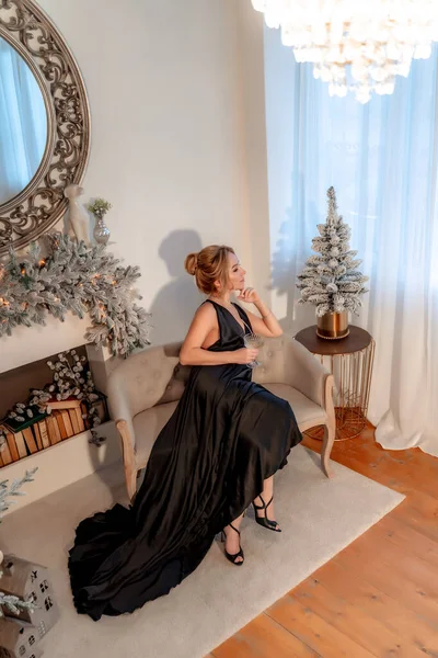 Портрет состоятельной зрелой женщины с вечерним макияжем и прической, позирующей в черном платье на фоне рождественской комнаты. Роскошный образ жизни. Косметология, пластическая хирургия, омоложение. — стоковое фото