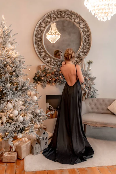 Portrait d'une femme mûre riche avec maquillage du soir et coiffure posant dans une robe noire sur fond de salle de Noël. Style de vie luxueux. Cosmétologie, chirurgie plastique, rajeunissement. — Photo