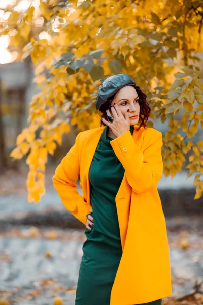 Krásná žena chodí na podzim ven. Má na sobě žlutý kabát a zelené šaty. Mladá žena si užívá podzimní počasí. Podzimní obsah. — Stock fotografie