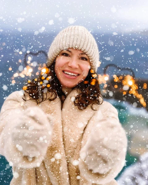 Retrato de invierno al aire libre de elegante mujer de mediana edad feliz sonriente en sombrero beige, abrigo de piel sintética ligera sosteniendo un bengala, posando sobre el fondo del mar y la nieve. —  Fotos de Stock