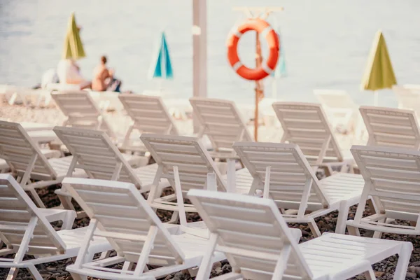 Várias espreguiçadeiras brancas e um guarda-chuva em uma praia deserta. O conceito de férias perfeito. — Fotografia de Stock