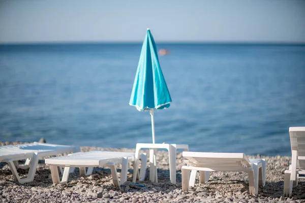 Several white sun loungers and a turquoise parasol on a deserted beach. The perfect vacation concept. — Stock Photo, Image