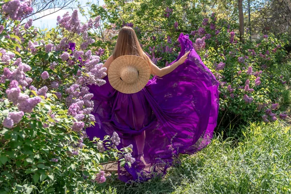 Modelo de moda en flores lila, Mujer joven en hermoso vestido largo ondeando en el viento, Retrato de belleza al aire libre en el jardín floreciente —  Fotos de Stock
