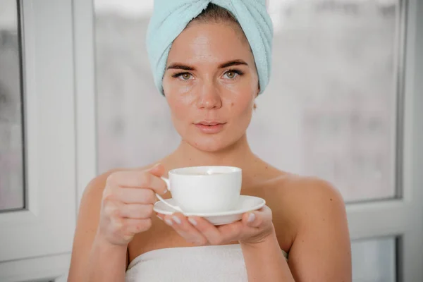 Jovem mulher relaxada serena em toalha de banho spa beber café de chá de bebida quente depois de tomar banho de chuveiro em casa. Tratamento de beleza, conceito de hidratação. — Fotografia de Stock