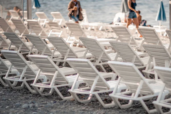 Néhány fehér napozó és egy esernyő egy elhagyatott tengerparton. A tökéletes nyaralás koncepciója. — Stock Fotó