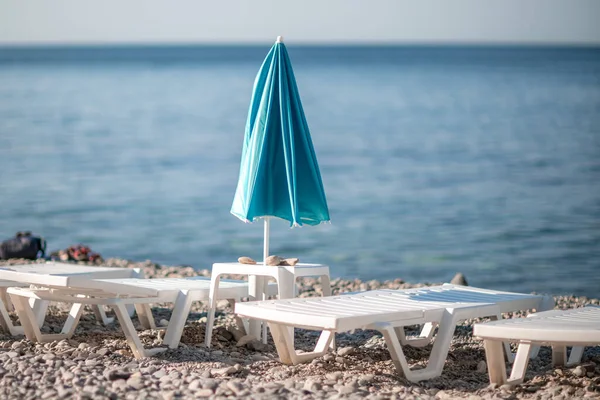 Várias espreguiçadeiras brancas e um guarda-sol turquesa em uma praia deserta. O conceito de férias perfeito. — Fotografia de Stock