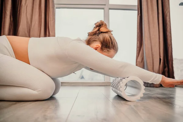 흰옷을 입은 성인 운동 선수인 여자 가 바닥에서 파시아 운동을 하고 있다 - 코카서스 여자가 안마 폼 롤러 - 등의 긴장을 완화하고 근육 통증을 완화하는 도구 - 를 사용하고 있다 — 스톡 사진
