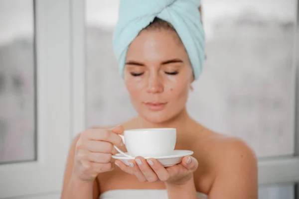 Jovem mulher relaxada serena em toalha de banho spa beber café de chá de bebida quente depois de tomar banho de chuveiro em casa. Tratamento de beleza, conceito de hidratação. — Fotografia de Stock