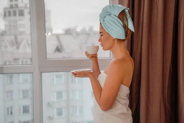 Joven mujer serena y relajada en toalla de baño de spa bebiendo café de té de bebida caliente después de tomar un baño de ducha en casa. Tratamiento de belleza, concepto de hidratación. — Foto de Stock