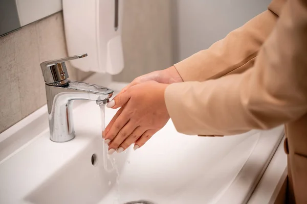 一名妇女在公共卫生间的自来水下洗手. — 图库照片