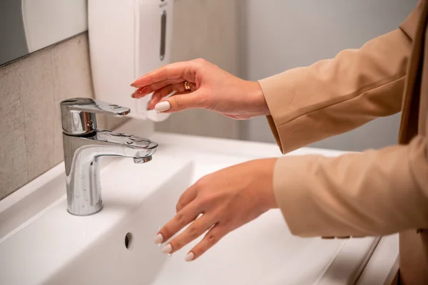 一名妇女在公共卫生间的自来水下洗手. — 图库照片