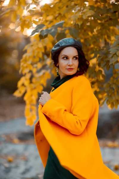 Hermosa mujer camina al aire libre en otoño. Lleva un abrigo amarillo y un vestido verde. Mujer joven disfrutando del clima otoñal. Contenido de otoño. —  Fotos de Stock