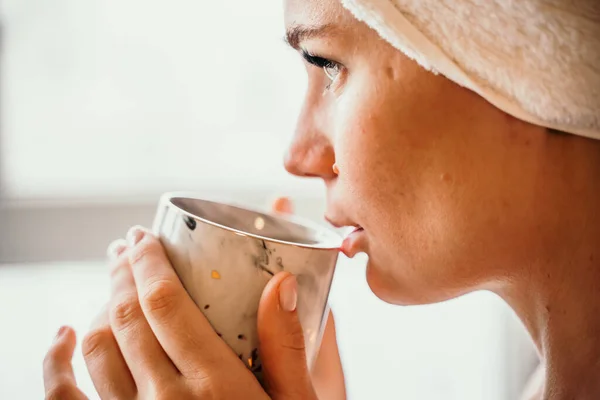 Joven mujer serena y relajada en toalla de baño de spa bebiendo café de té de bebida caliente después de tomar un baño de ducha en casa. Tratamiento de belleza, concepto de hidratación. — Foto de Stock