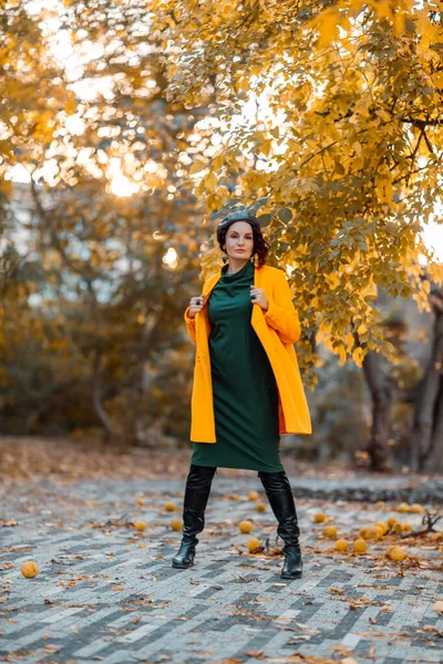 Hermosa mujer camina al aire libre en otoño. Lleva un abrigo amarillo y un vestido verde. Mujer joven disfrutando del clima otoñal. Contenido de otoño. —  Fotos de Stock