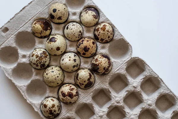 Spotted quail eggs in an egg box on a light background, natural eco-friendly products