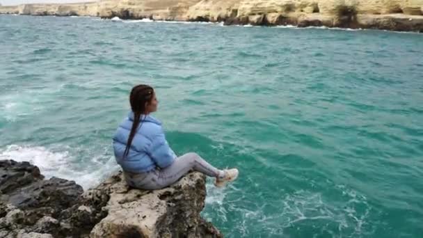 Женщина Синей Куртке Сидит Скале Над Скалой Над Морем Глядя — стоковое видео