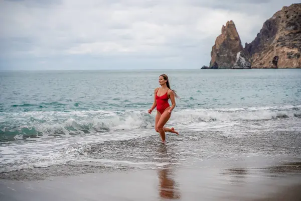波の泡の中で海岸に沿って実行され 小石のビーチで赤い水着で美しいとセクシーなブルネット — ストック写真