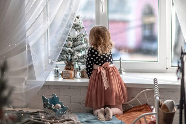 Mała Dziewczynka Siedzi Łóżku Przy Oknie Ozdabia Choinkę Małymi Świątecznymi Zdjęcie Stockowe