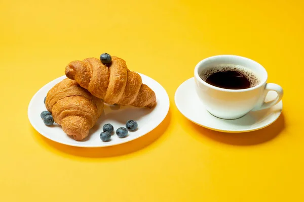 노란색 배경에 블루베리와 커피를 곁들인 프랑스 크로와 있습니다 유럽식 페이스트리 — 스톡 사진