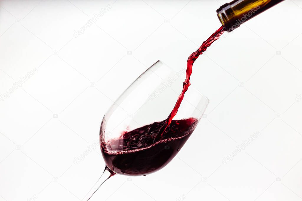 Red wine pouring in the glass on white background close up. Splashes and  drops of wine. Alcohol drink
