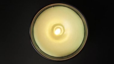 Siyah arka planda yanan aroma mumu. Mum ışığı, yüksek çerçeve üzerinde yakın çekim yapar. Bardakta yeşil aroma mumu yanıyor.