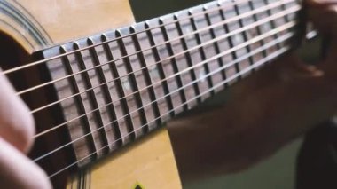 Akustik gitarı parmaklarıyla yavaş çekimde çalmak. Müzisyen evde yakın çekim gitar çalar.