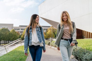 Üniversiteden iki bayan meslektaşın, güneşli bir günde kameraya bakıp sohbet etmelerinin ön görüntüsü..