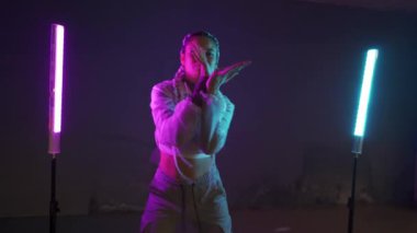 Genç kız park yerinde mor ve mavi neon ışıklarla dans ediyor. Genç bir kadın renkli ışıklarla modern funky dans koreografisi yapıyor.