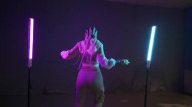 Genç kız park yerinde mor ve mavi neon ışıklarla dans ediyor. Genç bir kadın renkli ışıklarla modern funky dans koreografisi yapıyor.