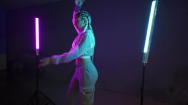 Genç kız park yerinde mor ve mavi neon ışıklarla dans ediyor. Genç bir kadın renkli ışıklarla modern funky dans koreografisi yapıyor.