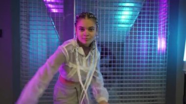 Genç kız park yerinde mor ve mavi neon ışıklarla dans ediyor. Genç bir kadın renkli ışıklarla modern funky dans koreografisi yapıyor.