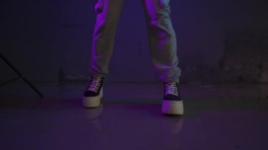 Genç kız park yerinde mor ve mavi neon ışıklarla dans ediyor. Genç bir kadın modern funky dans koreografisi yapıyor ayaklarıyla ve renkli ışıklarıyla.