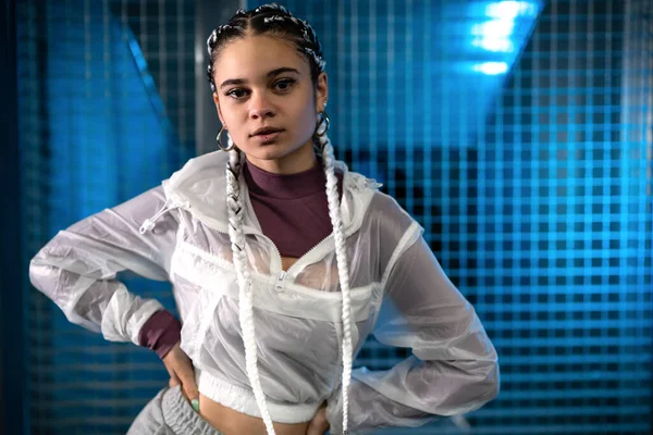 Mujer joven posando con las manos en la cintura y mirando a la cámara con fondo con luz azul — Foto de Stock