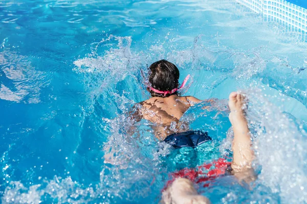 Rear view of unrecognizable child playing in a small removable pool of a house. Child swimming in the water. High quality photo