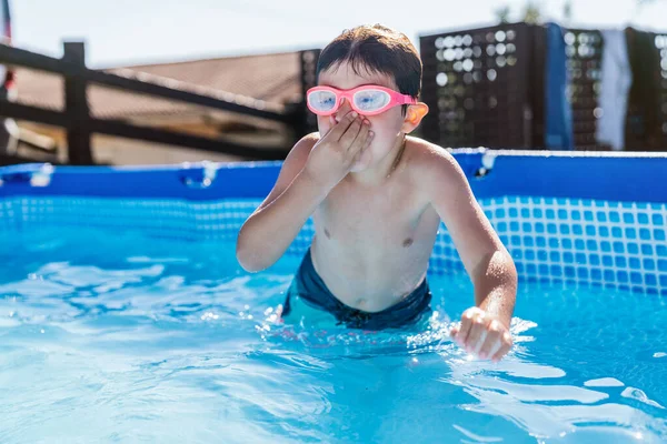 Child playing in a small removable pool in a house. Child diving head first into the water with his hands covering his nose. High quality photo